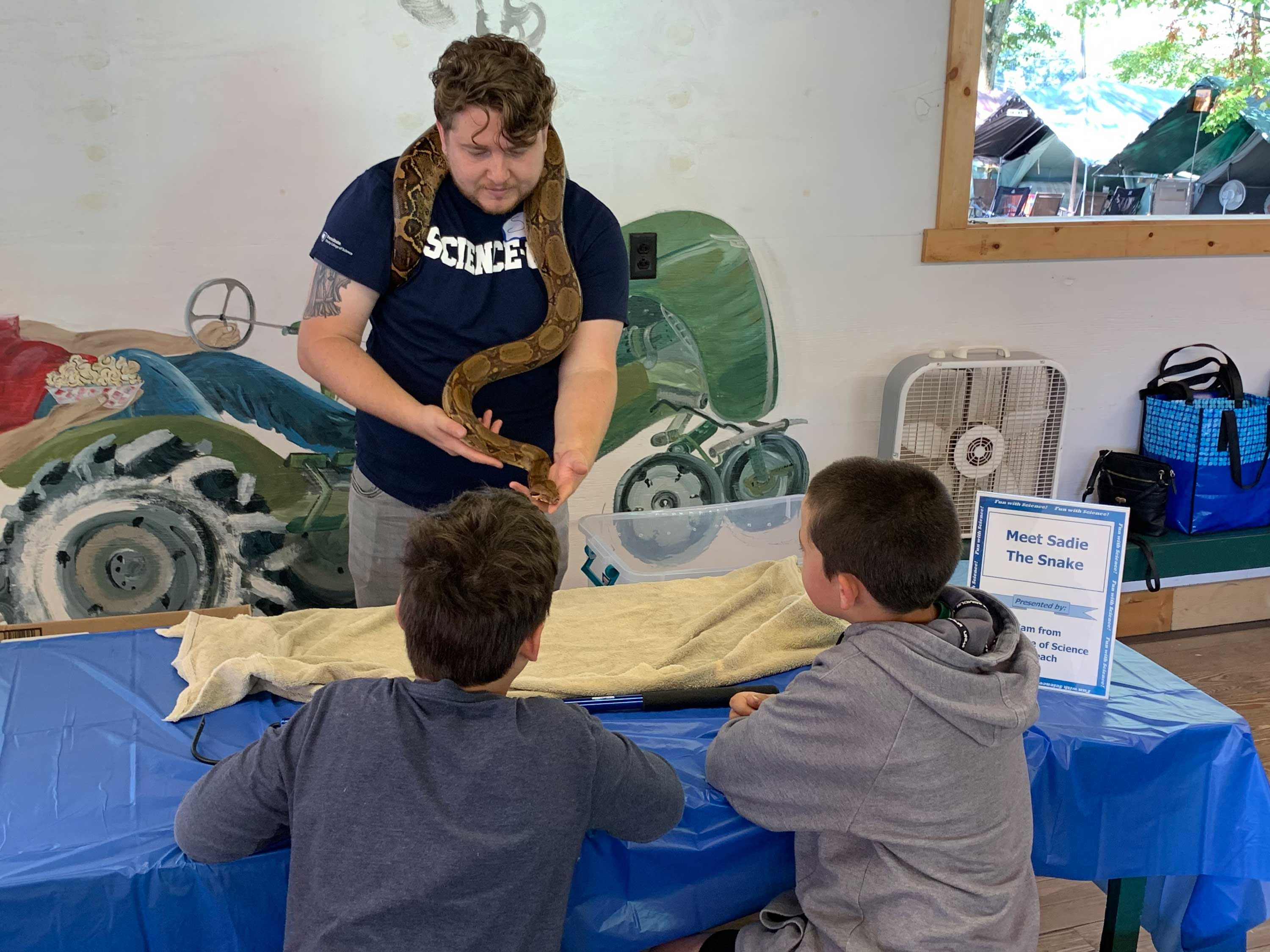 man in penn state shirt holds snake in front of kids