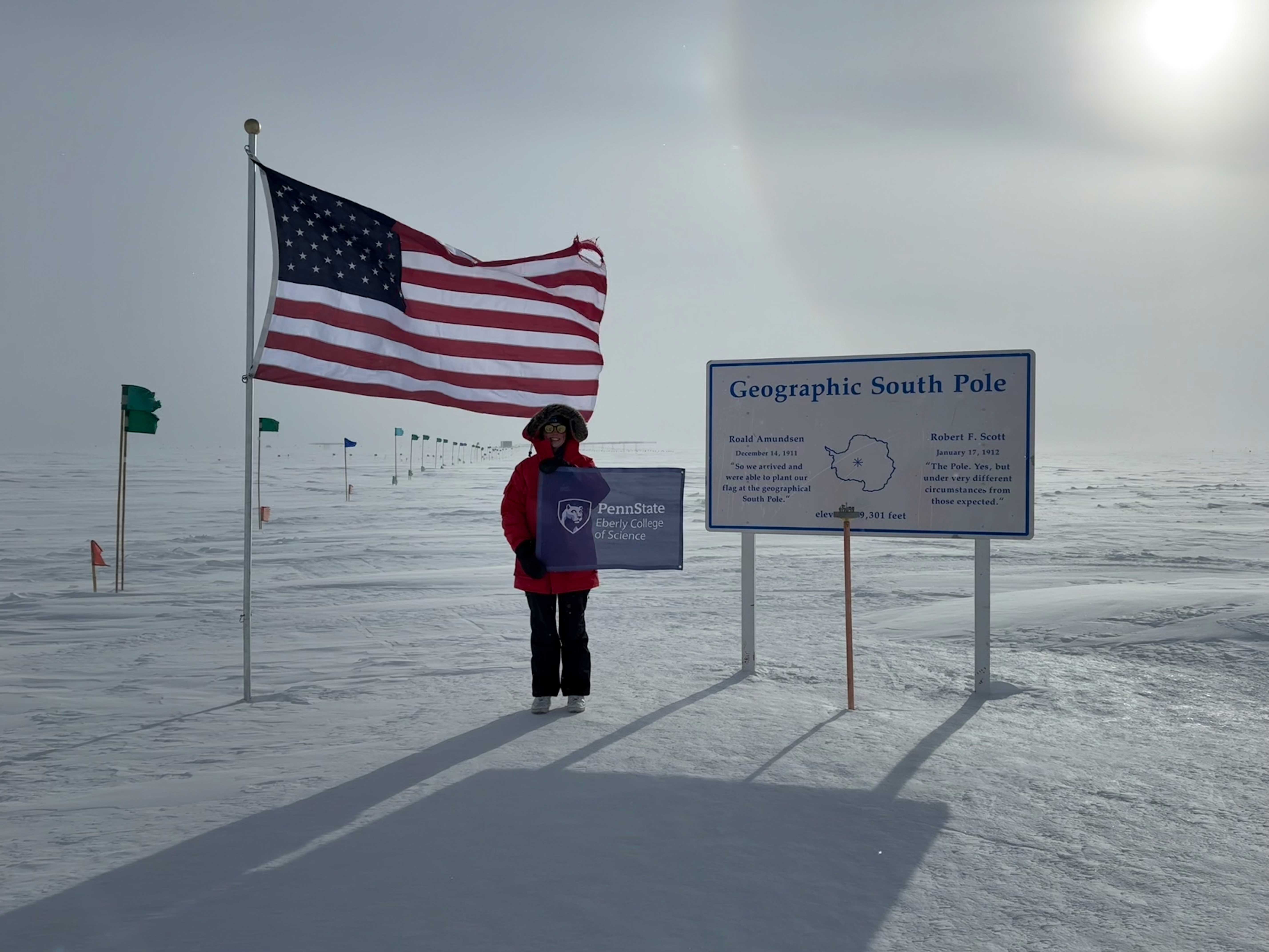 Kayla DeHolton holds an Eberly College of Science flag at the South Pole