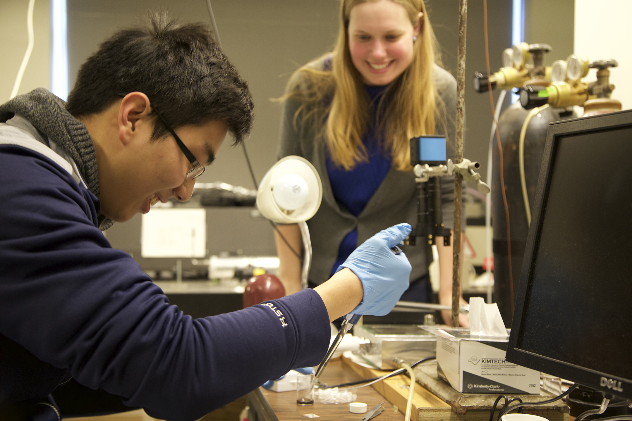 Student working at a lab bench while another student looks on