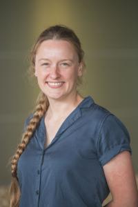 A person with a long braid wearing a blue shirt. The background features a gradient from dark to light green.