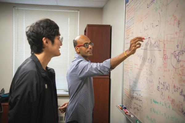 Bharath Sriperumbudur writes on white board while student looks on