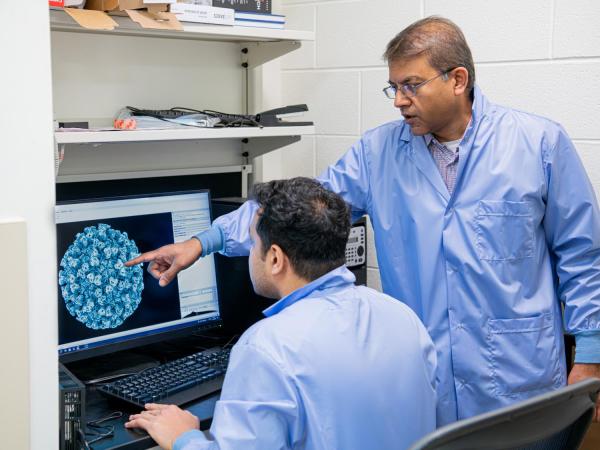 Ganesh Anand with one of his students pointing at a screen with a virus being displayed. 