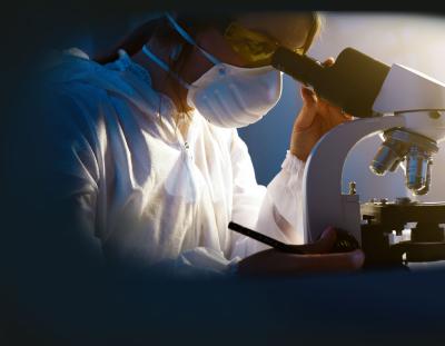 woman wearing mask looking through microscope