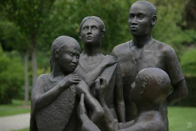 Bronze statue of health worker giving vaccine to one person as two others look on.
