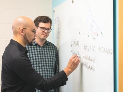 Matthew Williams writes on white board while Christian Huber watches