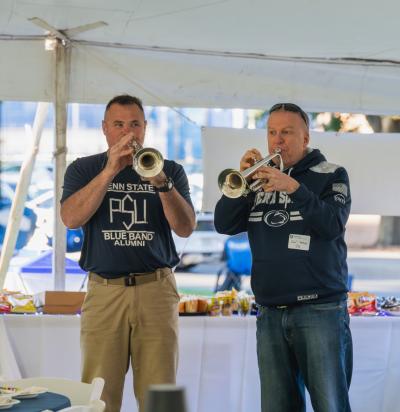Two gentlemen in blue Penn State gear playing trumpets at the Penn State Homecoming tailgate.