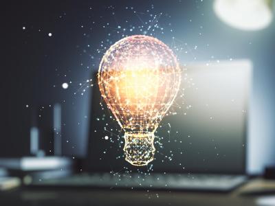 Digital illustration of a glowing light bulb made of interconnected lines and nodes, floating in front of a blurred laptop screen, symbolizing innovation and ideas.