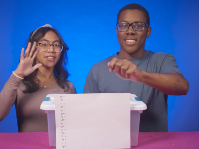 Two students hold bouncy balls over a plastic tub