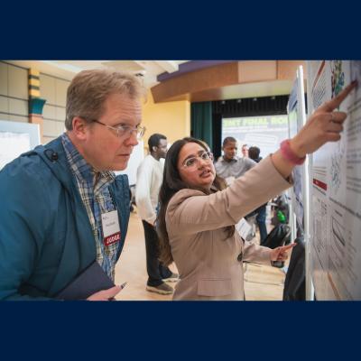 Avanti Valragkar pointing at her poster for the Graduate Exhibition to a judge.