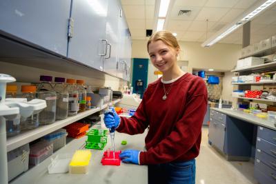 Person working at a laboratory bench using a pipette, with labeled bottles and lab equipment nearby.