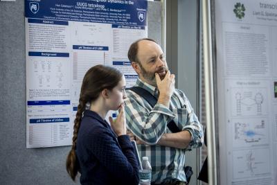 Two attendees stand by research poster, reading and discussing data displayed on a scientific poster board.