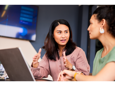 woman sitting at computer listing to another woman