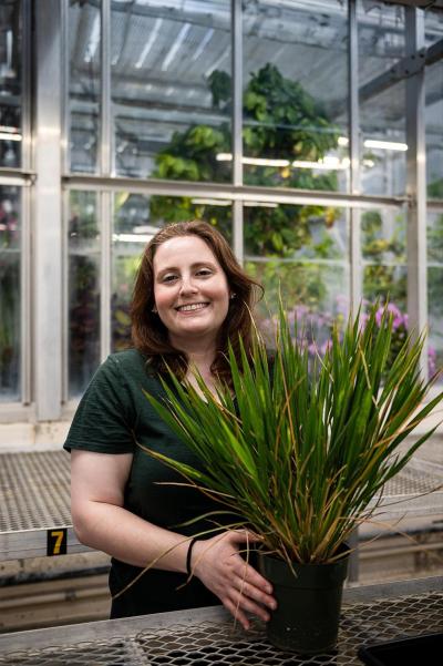 Jessica Walnut holding a large potted plant inside a greenhouse