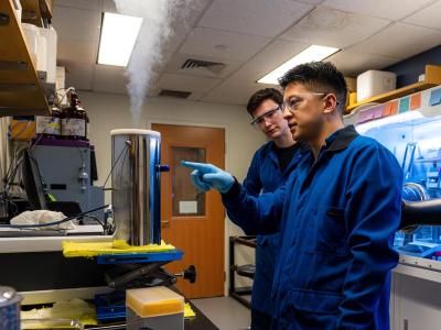 Jonathan Kuo and Alexander Arnette wearing lab coats pointing at lab bench