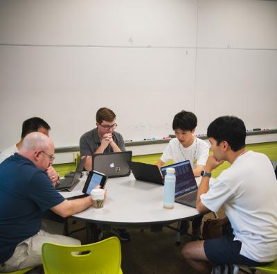 several students and researchers sit at table and look at their laptops