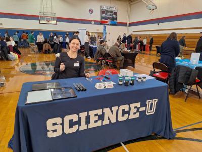 student sitting at table with Science-U tablecloth in school gym