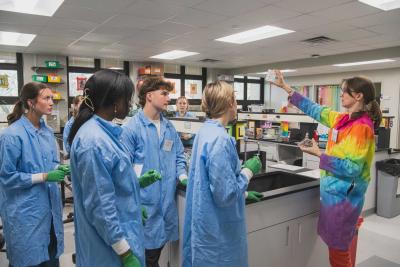 Carly Sjorgren shows lab sample to group of students wearing lab coats
