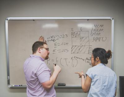 Noah Feldman draws on white board while speaking to a woman