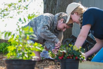 two students dig in dirt with potted plants in foreground