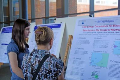 A student reviews her physics research project during the REU Symposium poster session.
