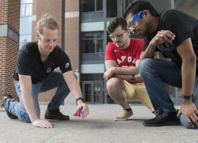 Drew Veenis, left, places a rocket on a hard surface while fellow graduate students Ryan Szukalo and Varun Mandalaparthy look on. Credit: Patrick Mansel