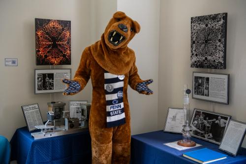The Nittany Lion poses with paws out beside two pieces of historic microscope equipment used by Professor Emeritus Erwin Müller.