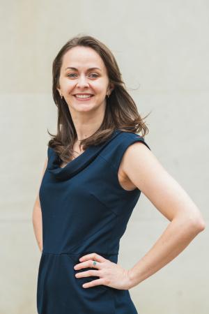 Person in a sleeveless navy dress stands with one hand on a hip against a light, neutral background.