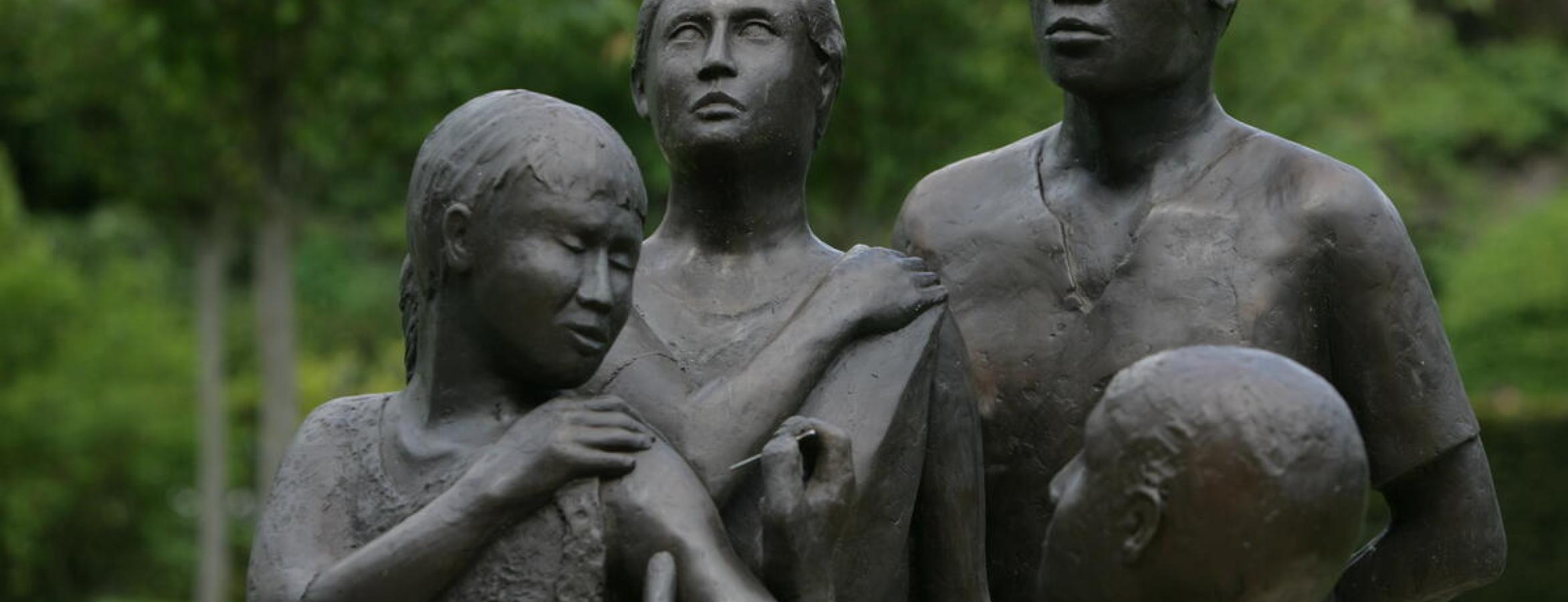 Bronze statue of health worker giving vaccine to one person as two others look on.