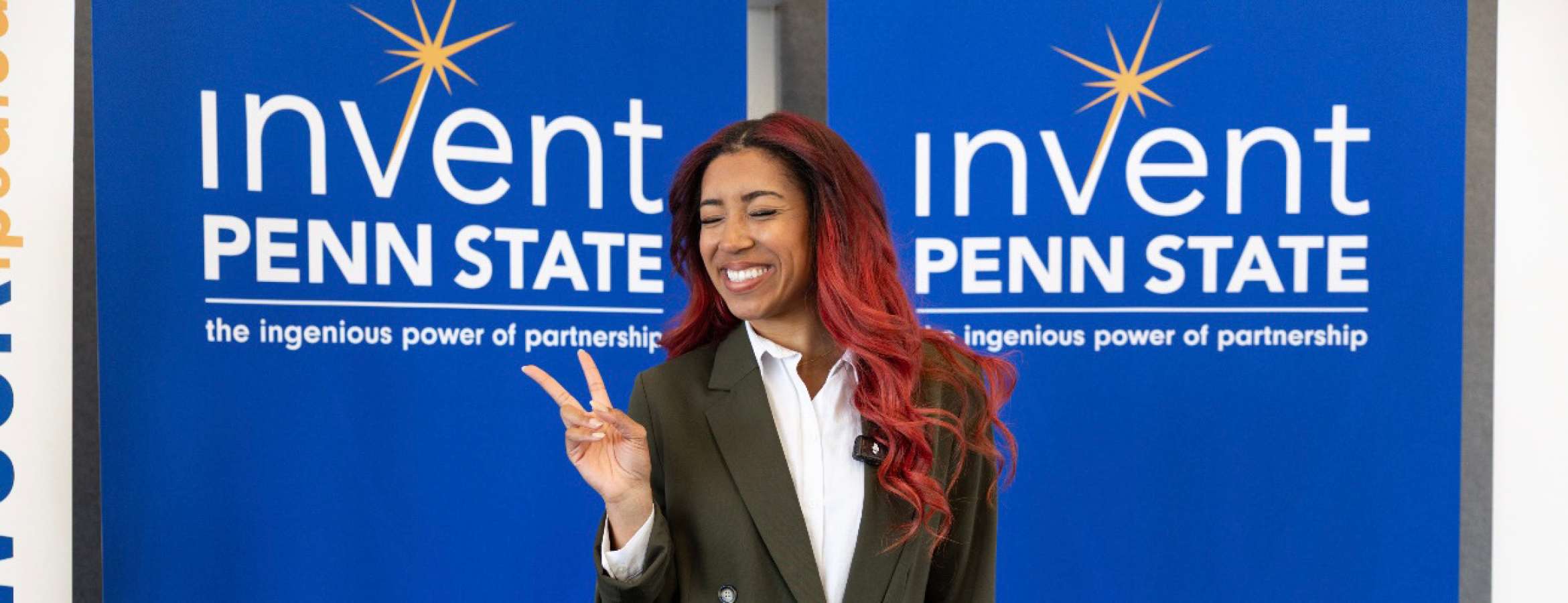 Haley McClain Hill posing for a photo in front of two signs that read "Invent Penn State."