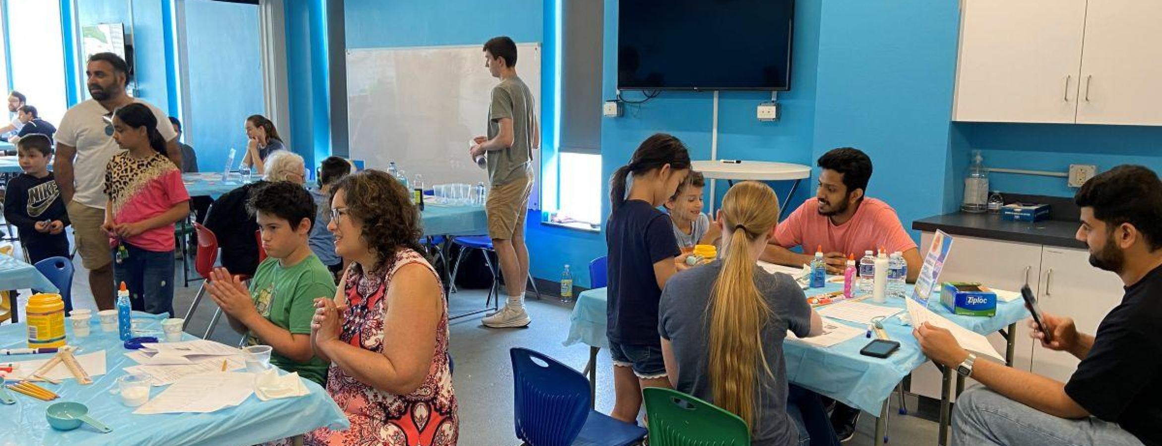 group of young students standing around tables working on science projects
