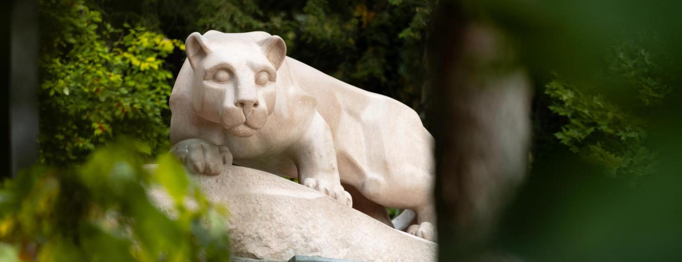 nittany lion statute through green foliage