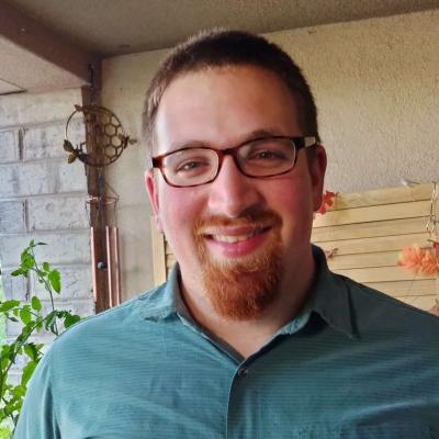 Noah Feldman's Headshot. A smiling man shown from the shoulder's up. He has brown glasses, short auburn hair, and a small beard around his mouth. 