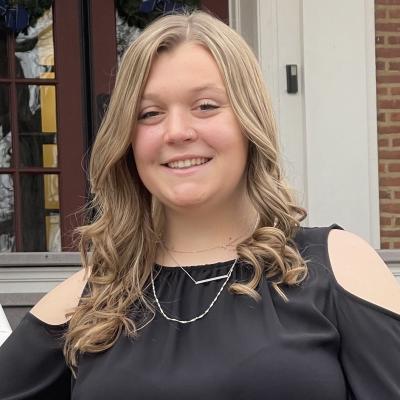 Headshot of Cati Besch smiling, standing on steps in front of a campus building. 