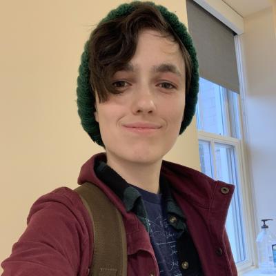 A photograph of Svetlana Pack wearing a green knit hat and a red jacket. They are smiling