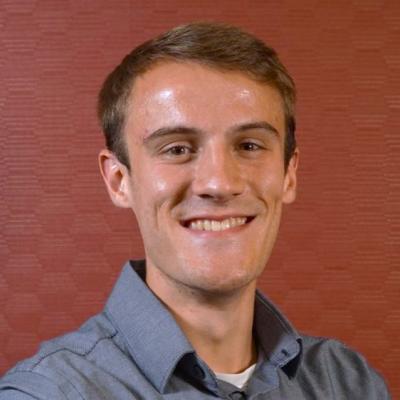 portrait of Brandon Radzom smiling in front of a redish background