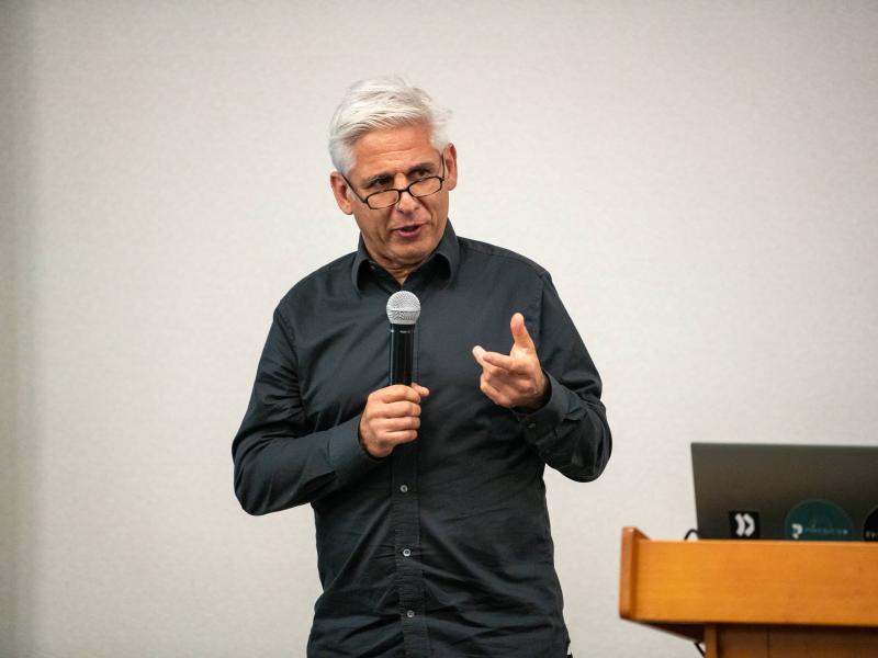 Robin Tuluie holds microphone while presenting a talk
