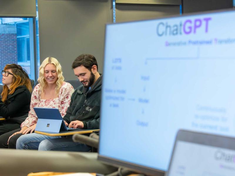 computer with ChatGPT slide in foreground with Morgan Vincent and students in back