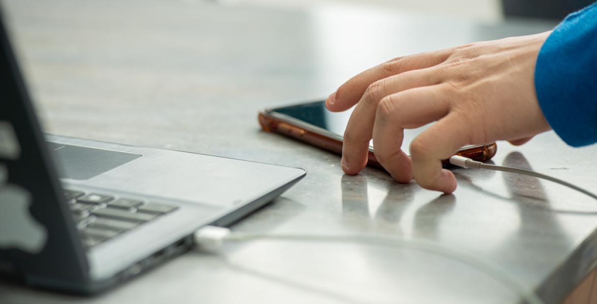 A hand reaches for a smartphone sitting on a table.