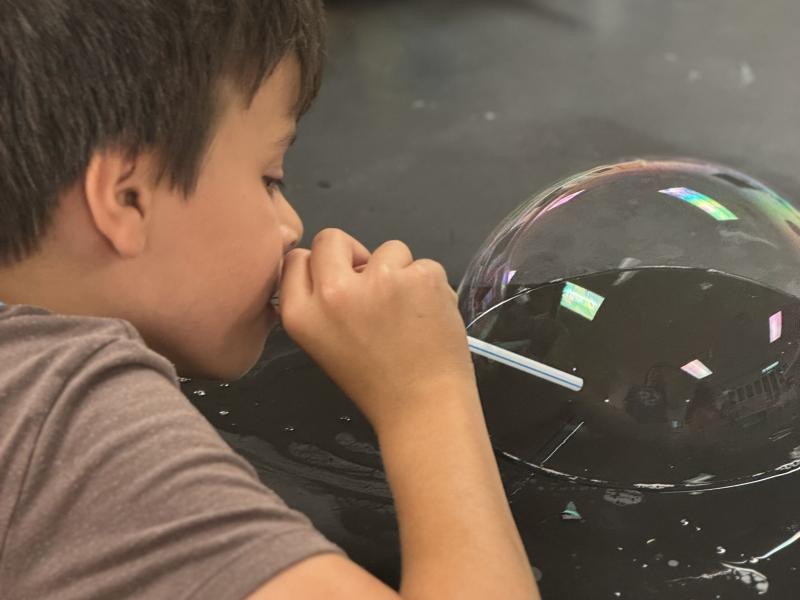 Science-U camper blowing a bubble on a countertop lab bench
