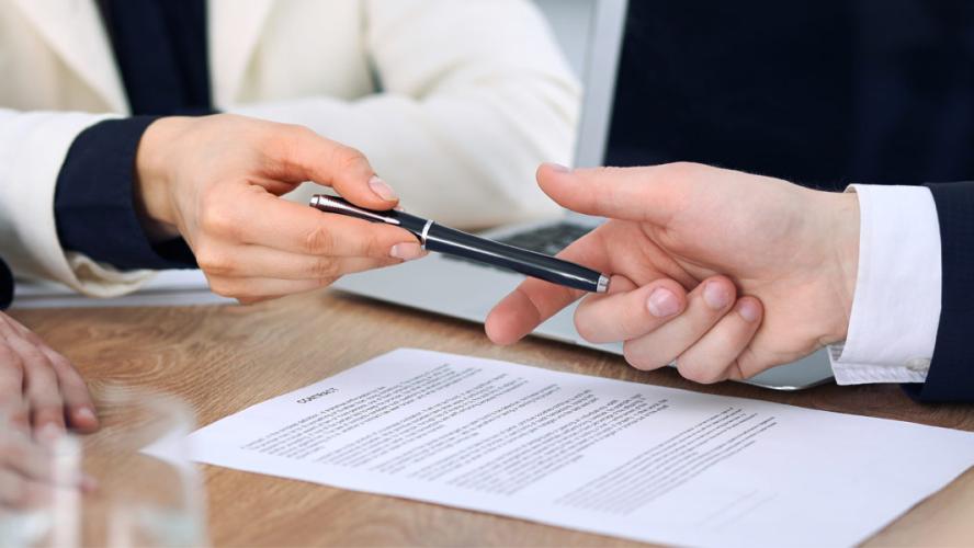 A business woman handing a pen to a business man to sign a contract.