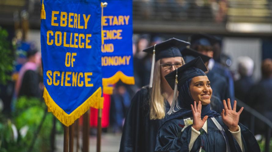 A new alumna waves to the crowd at the 2023 spring commencement ceremony.