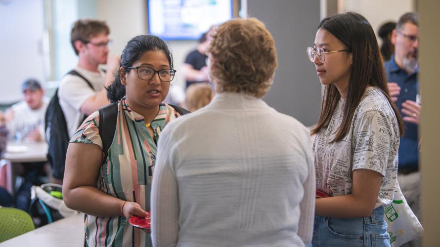 Two coeds speaking to a faculty member during the Eberly Student Council networking event.