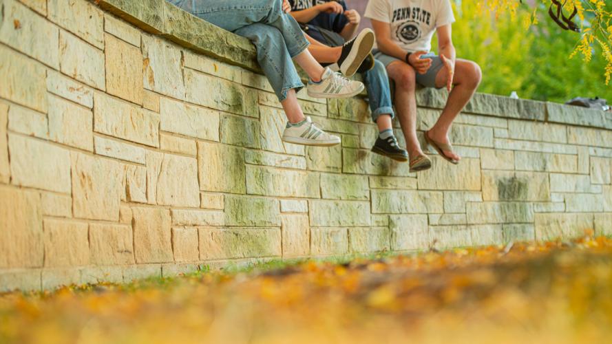 A group of four students sitting on a wall talking to each other at the University Park campus.