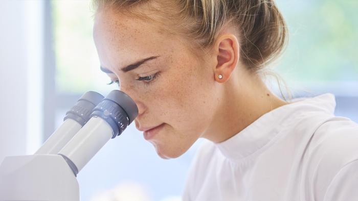 A woman with blonde hair looking through a microscope.