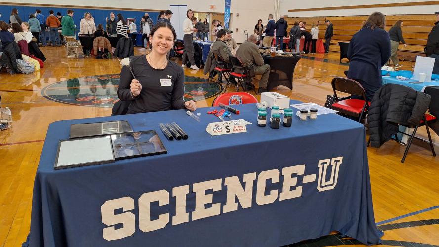 student sitting at table with Science-U tablecloth in school gym