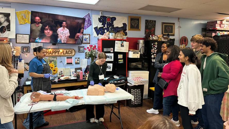 student looks at CPR dummy on table while other students look on