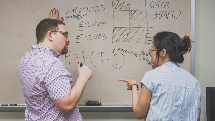 Noah Feldman draws on white board while speaking to a woman