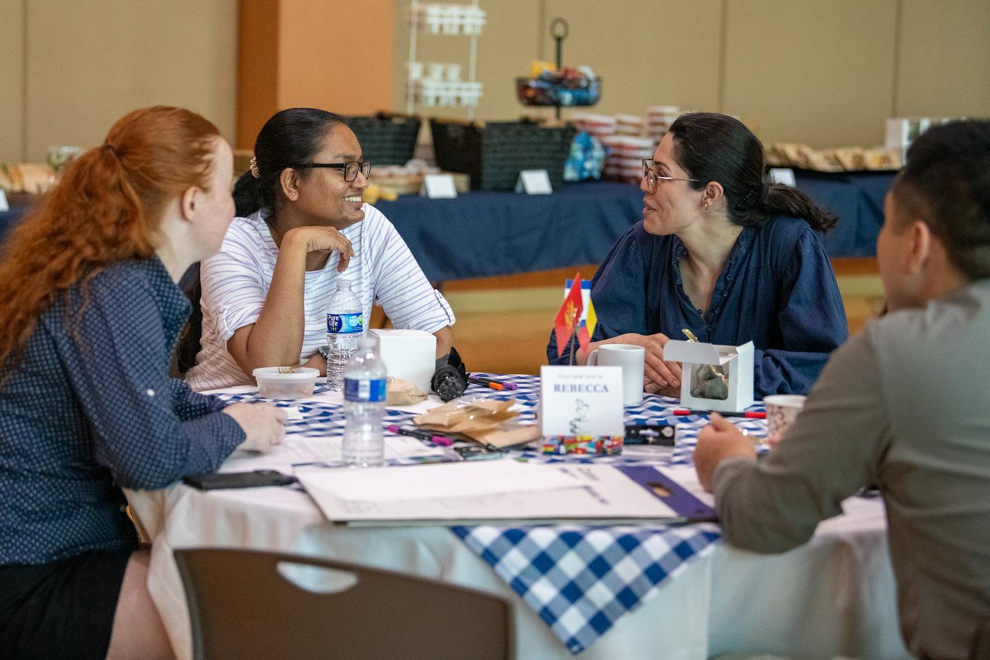 A group of four people sitting at a table and talking during the World Cafe event held at the HUB-Robeson Center