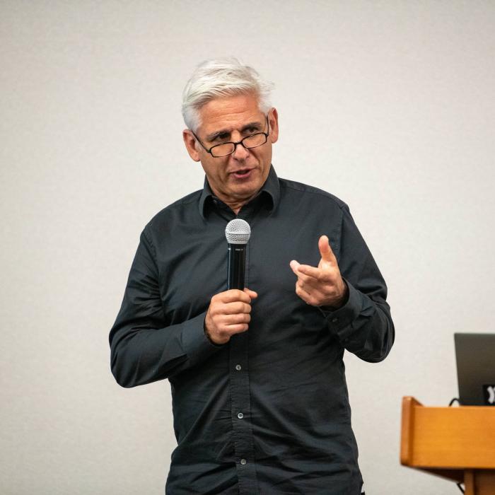 Robin Tuluie holds microphone while presenting a talk