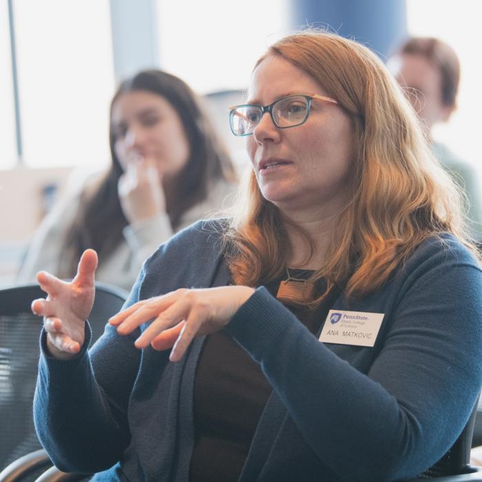 A female faculty member with shoulder-length red hair asking a question during a college conference.
